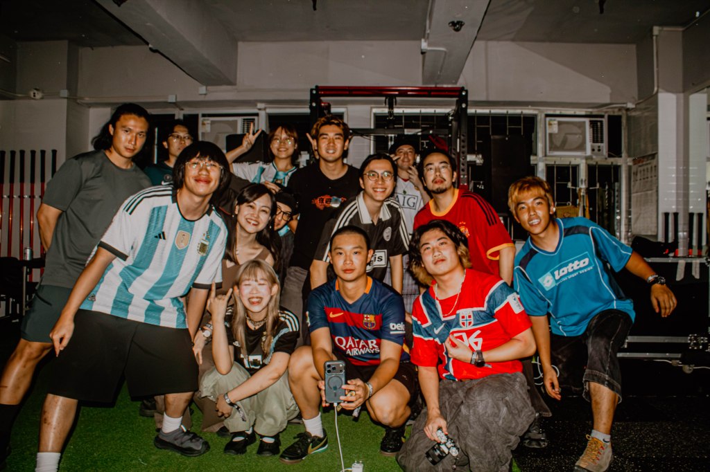 Group of friends posing together in a gym, wearing various football jerseys and smiling, with gym equipment in the background.